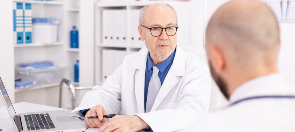 Experienced mature doctor explaining patient diagnosis to young medical physician during conference. Clinic expert therapist talking with colleagues about disease, medicine professional.